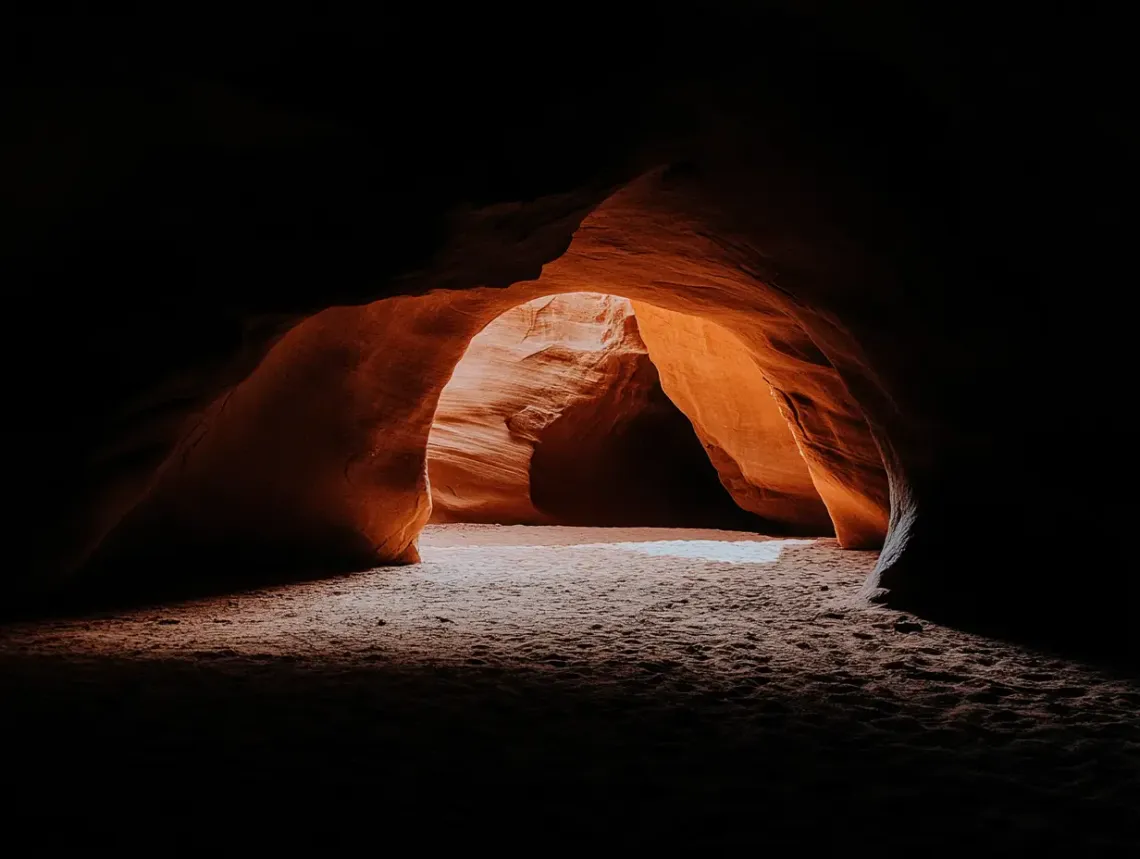 Dramatic image of a dark, rough-walled cave, illuminated by a single ray of light from above. 