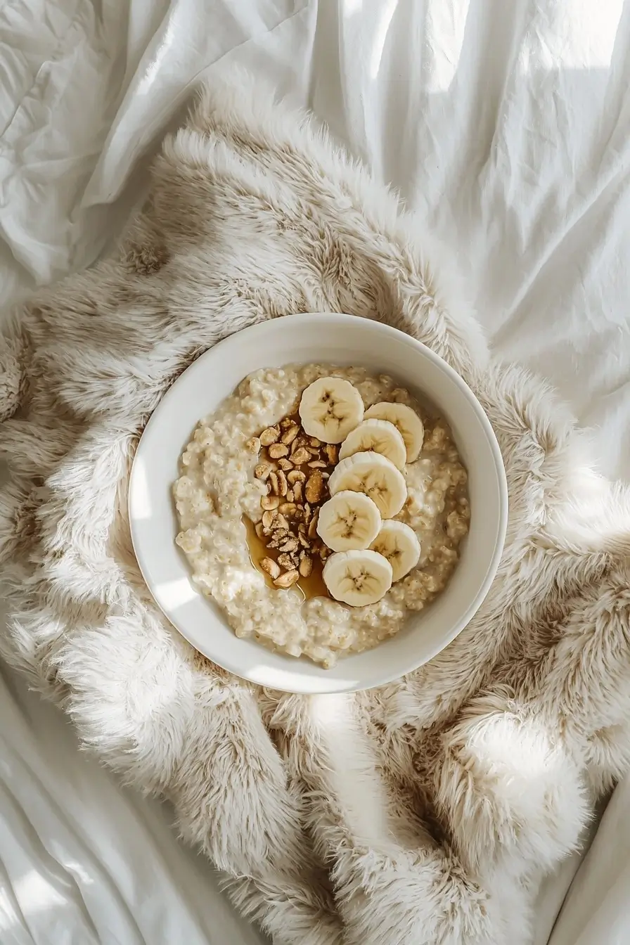 Top-down view of a breakfast bowl of creamy oatmeal topped with banana slices and sprinkled nuts.