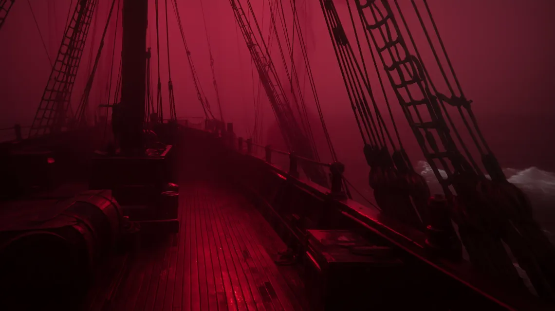 Ship on water with red light on deck, conveying a sense of calmness and mystery against a dark background.